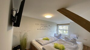 A bedroom with a bed, pillows, a wall-mounted TV, a window, and a decorative wall with text. - Holiday home "On the cliffs" Apt. 3 (Boltenhagen Redewisch)
