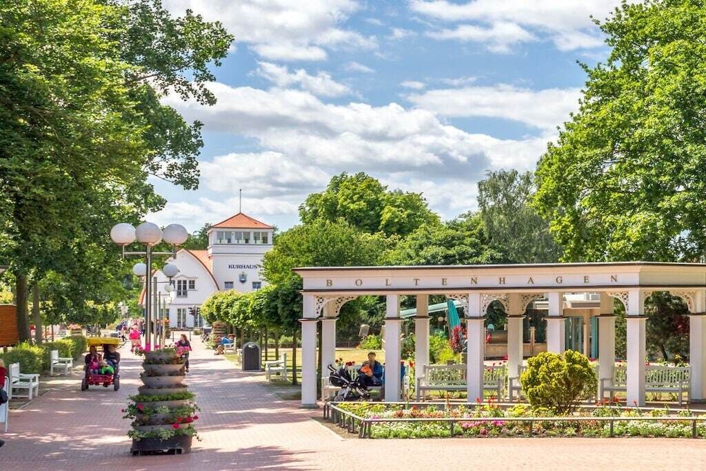 Um parque com um coreto identificado como 'BOLTEENHAGEN' e um edifício com telhado vermelho ao fundo.