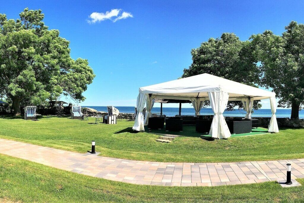 A tented outdoor area with a paved walkway, seating, and a view of the sea.