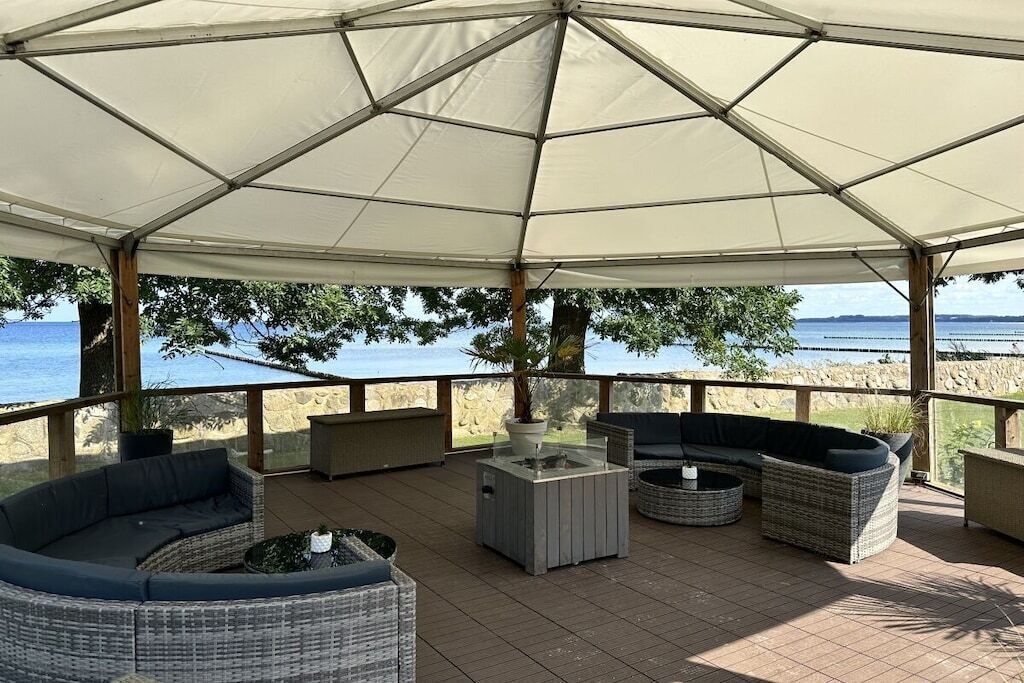 Un patio exterior con un gran paraguas, mobiliario de mimbre y vistas al mar.