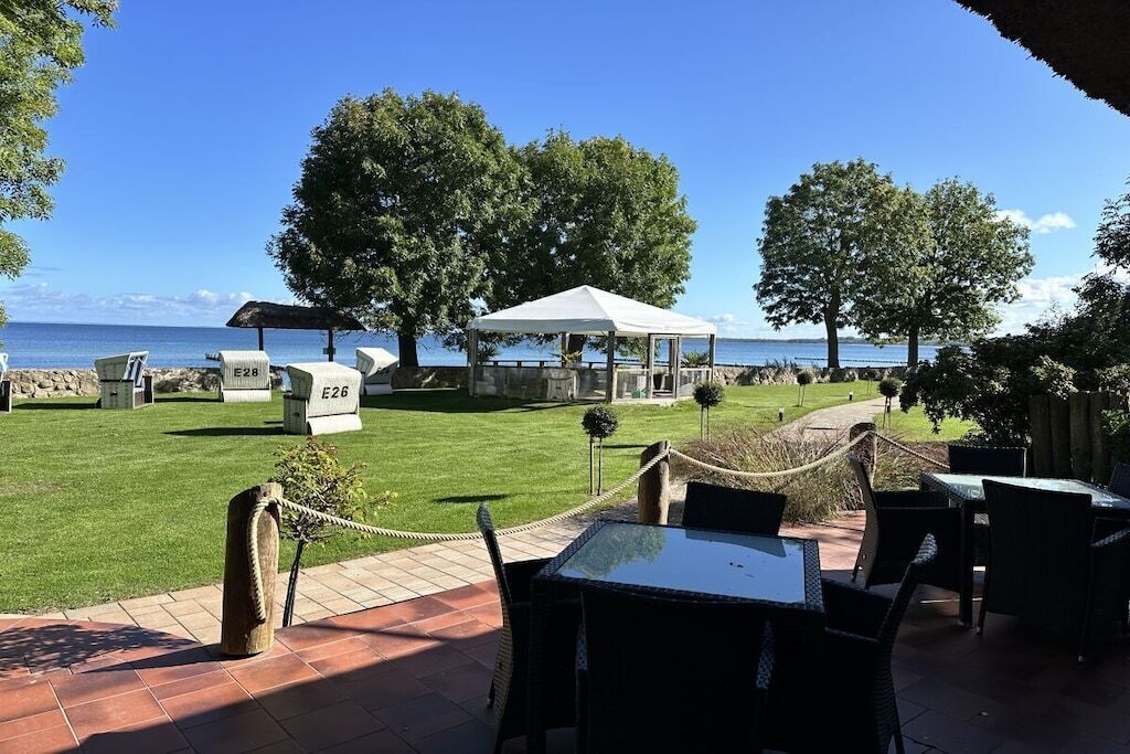 An outdoor seating area with tables and chairs, a covered pavilion, and a view of the sea.