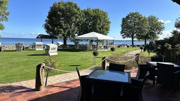 An outdoor seating area with tables and chairs, a covered pavilion, and a view of the sea. - Holiday home "On the cliffs" Apt. 3 (Boltenhagen Redewisch)