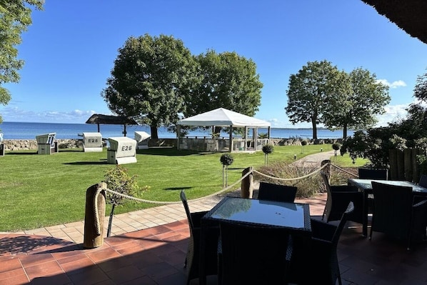 Un espacio exterior con mesas y sillas, un pabellón cubierto y vistas al mar.