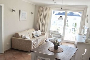 A living room with a sofa, a dining table with a vase, and a view through a glass door. - Apartment Residence Baltic Sea Beach (Kühlungsborn)