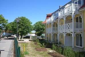 A yellow building with white balconies and a red roof, surrounded by greenery and a paved path. - Apartment Residence Baltic Sea Beach (Kühlungsborn)