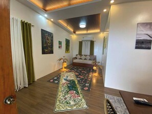 A bedroom with a wooden floor, a large floral rug, a bed with white bedding, and a painting on the wall.