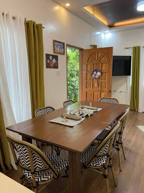 A dining area with a wooden table set for four, surrounded by chairs with patterned cushions.
