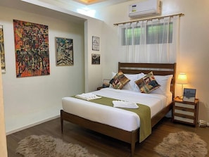 A neatly made bed with a green bedspread and white linens, a wooden headboard, and a nightstand with a lamp and a framed picture.