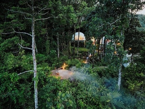 A forested area with a dome-shaped structure, a fire pit, and a pathway.