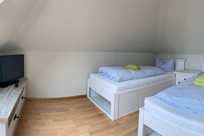 A bedroom with a TV on a wooden dresser, two beds with white bedding, and a sloped ceiling. - Holiday home "On the cliffs" Apt. 4 (Boltenhagen Redewisch)