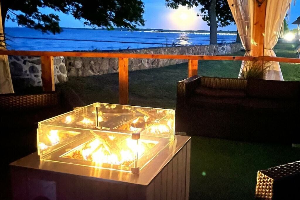 Un espace extérieur aménagé avec des tables et des chaises à plateaux en verre, offrant une vue sur une étendue d’eau.