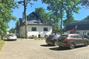 Una casa de dos pisos con entrada pavimentada y autos estacionados.