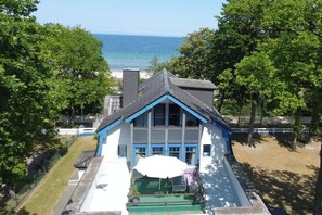A two-story house with a blue and white exterior, a front porch with a green bench, and a view of the ocean. - Beach villa Miramare, apartment Seezunge (Ostsee Bad Boltenhagen)