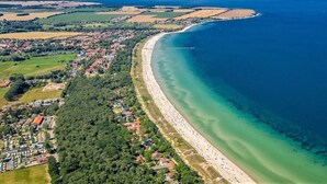 Vista aérea de un pueblo costero con una playa extensa y arenosa, abundante vegetación y un mar azul y despejado.