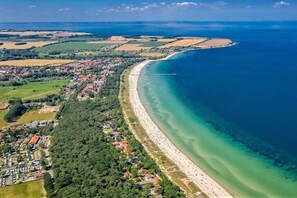 Vista aérea de un pueblo costero con una playa extensa y arenosa, abundante vegetación y un mar azul y despejado.