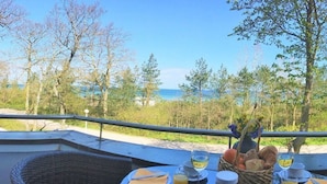 Una mesa lista para el desayuno con vistas al mar, una silla de mimbre y una cesta de pan.