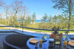 Una mesa lista para el desayuno con vistas al mar, una silla de mimbre y una cesta de pan.