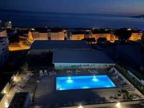 Ein Pool auf dem Dach mit Liegestühlen, umgeben von Gebäuden mit warmer Beleuchtung.