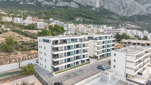 Ein mehrstöckiges Wohngebäude mit Balkonen, einem Parkplatz und einer Bergkulisse im Hintergrund.