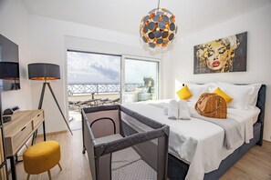 Ein Hotelzimmer mit Bett, Schreibtisch, Stuhl, Balkon mit Aussicht und einem Bild an der Wand.