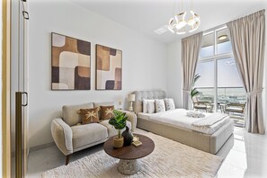 A modern bedroom with a sofa, a bed, a round coffee table, and artwork on the wall. - Stunning Studio | 12 Min to Mall of the Emirates (Dubai)