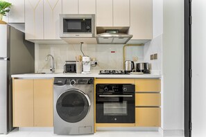 A modern kitchen with a washing machine, oven, microwave, and coffee maker. - Stunning Studio | 12 Min to Mall of the Emirates (Dubai)