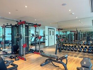 A gym with weightlifting equipment, treadmills, and a mirror reflecting the space. - Stunning Studio | 12 Min to Mall of the Emirates (Dubai)