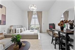 A modern hotel room with a bed, sofa, TV, and a view of the city. - Stunning Studio | 12 Min to Mall of the Emirates (Dubai)