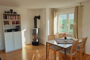 Ein Essbereich mit Tisch, Stühlen, einem Bücherregal und einem Kaminofen.
