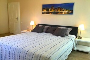 Una cama bien hecha con una colcha estampada, dos lámparas de noche y un cuadro con una vista urbana en la pared.