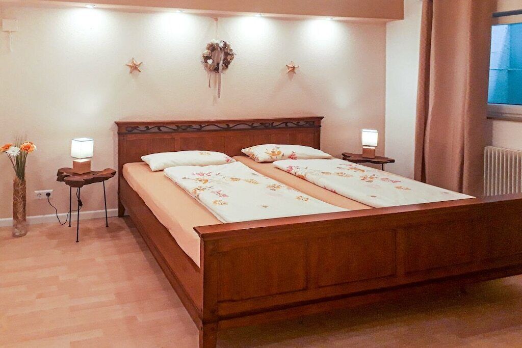 Ein Schlafzimmer mit einem hölzernen Bett, zwei Nachttischen mit Lampen, einer Wanddekoration und einem Fenster mit Vorhängen.