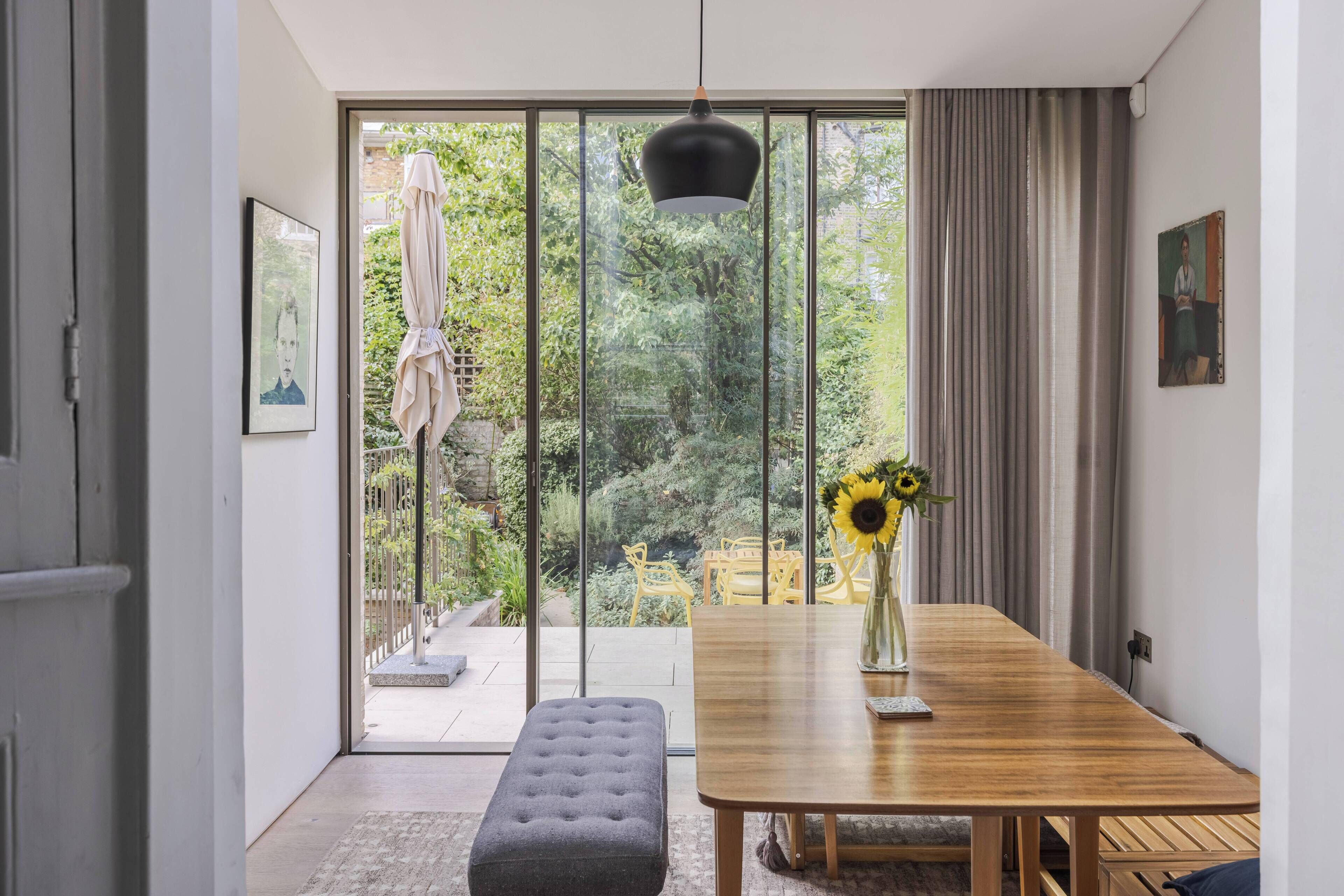 A modern dining area with a wooden table, bench, and a vase with sunflowers.