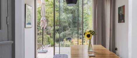 A modern dining area with a wooden table, bench, and a vase with sunflowers.
