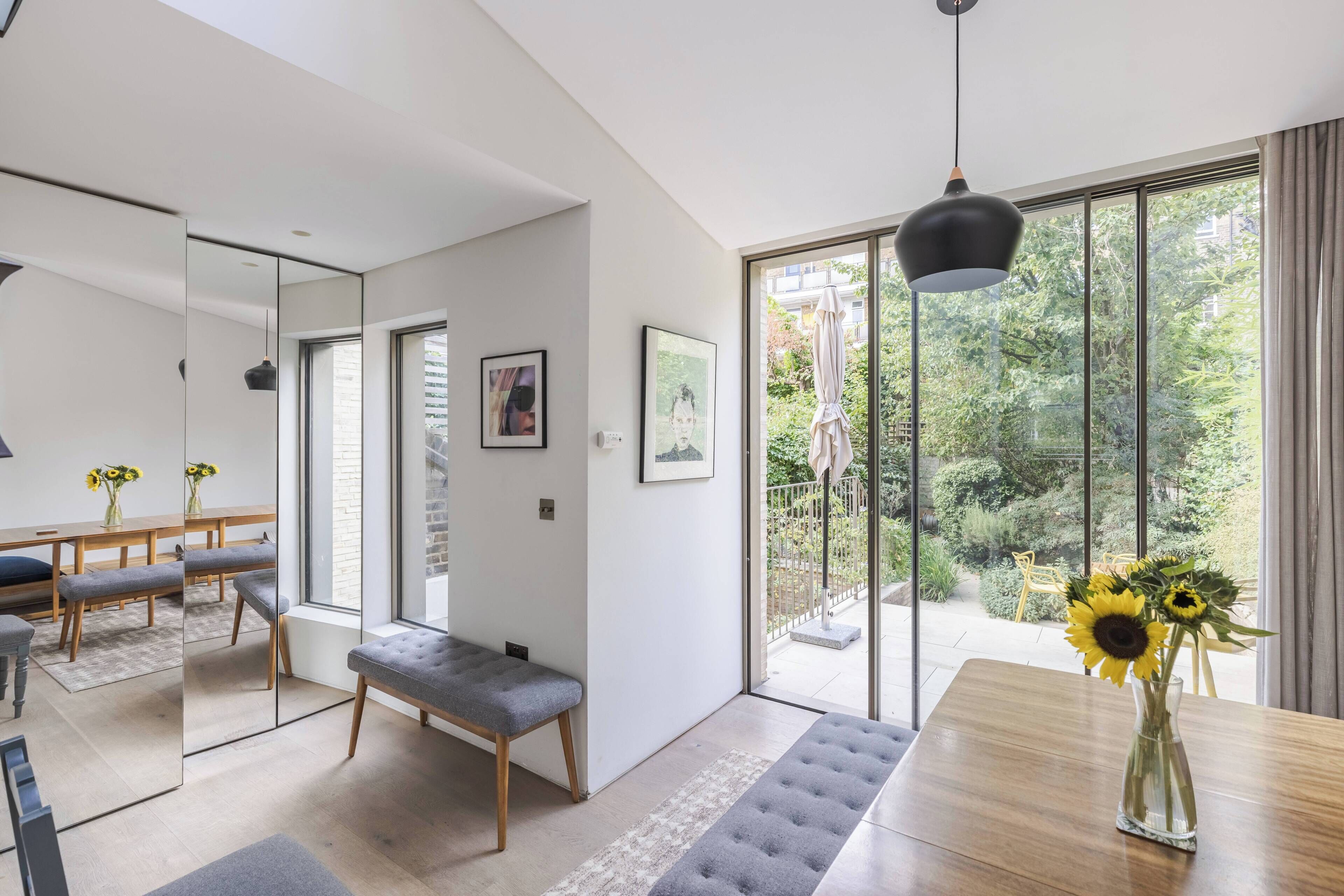 A modern interior with a dining area, bench, and large windows offering a view of the outdoors.