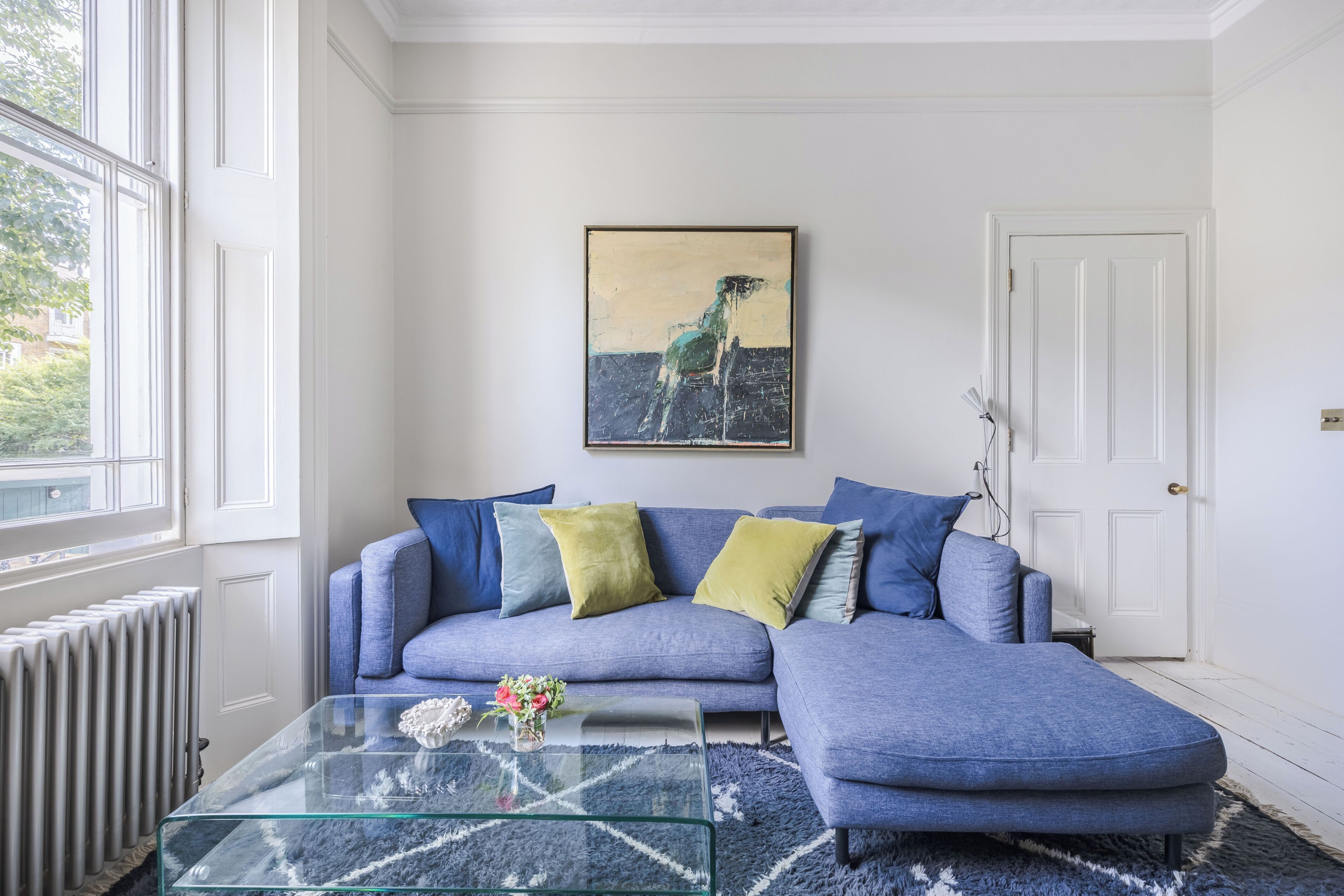 Un salon avec un canapé bleu, une table basse en verre et un tableau accroché au mur.