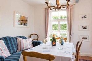 A dining area with a table set for two, a blue-striped sofa, and a chandelier. - Holiday home with 2 bedrooms (Krummhörn)