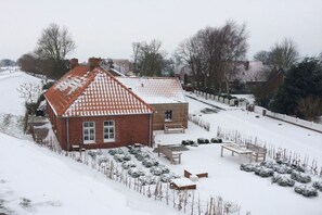A residential property with a sloped roof, a brick exterior, and a snow-covered garden with benches. - Holiday home with 2 bedrooms (Krummhörn)