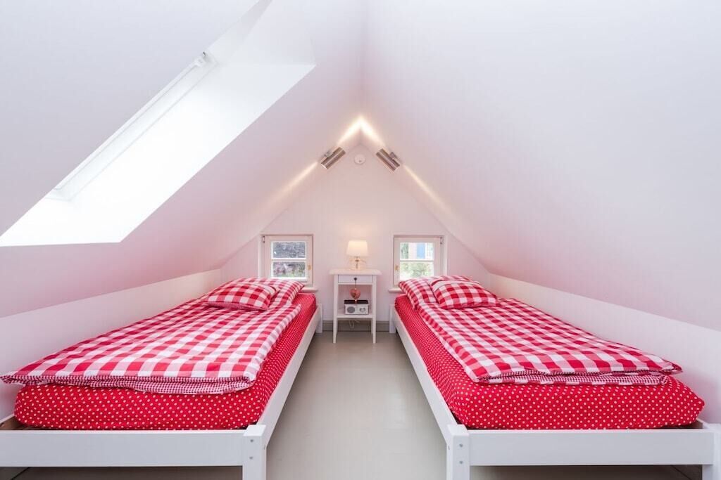 A small, triangular attic bedroom with two single beds, a nightstand, and a lamp.
