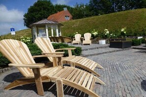 Outdoor wooden chairs and a gazebo on a paved area with a grassy hill in the background. - Holiday home with 2 bedrooms (Krummhörn)