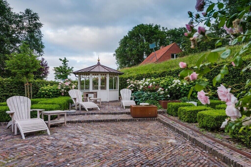Ein Garten mit einer Patio, einem Gazebo, weißen Stühlen und einem Ziegelweg.