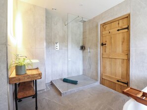 A modern bathroom with a shower, a wooden door, and a small wooden table with a plant. - Bridge Farm (Wrexham)
