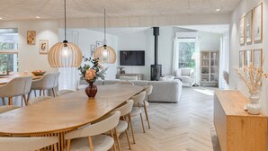 Ett modernt vardagsrum med en matplats, med ett stort träbord, bekväma sittplatser och en öppen spis.
