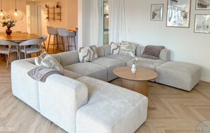 Un salon moderne avec un canapé d’angle, une table basse ronde et un coin repas comprenant des chaises et une table.