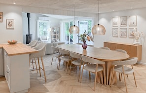 A modern kitchen with a wooden island, a dining area with a round table and chairs, and a view of the outdoors through large windows.