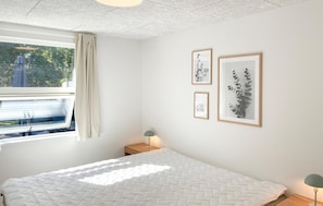 A bedroom with a bed, a window with curtains, and three framed pictures on the wall.