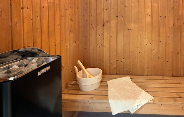 A sauna room with a black sauna heater, a wooden bowl, and a towel on a wooden bench.
