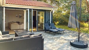 En uteplats med utemöbler, ett parasoll och en skjutdörr i glas som leder in till ett rum med en soffa och ett matbord.