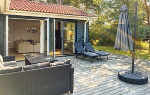 Une terrasse dotée de mobilier d’extérieur, d’un parasol et d’une porte-fenêtre coulissante donnant sur une pièce comprenant un canapé et une table à manger.