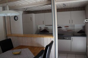 A compact kitchen with white cabinets, a wooden countertop, and a dining area with a table and chairs. - Holiday home with 2 bedrooms (Mirow - Granzow)