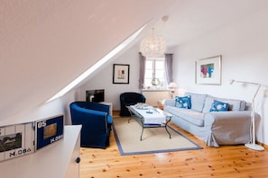 A modern living room with a blue sofa, a dining table, and a chandelier. - Holiday apartment with 1 bedroom (Krummhörn - Greetsiel)